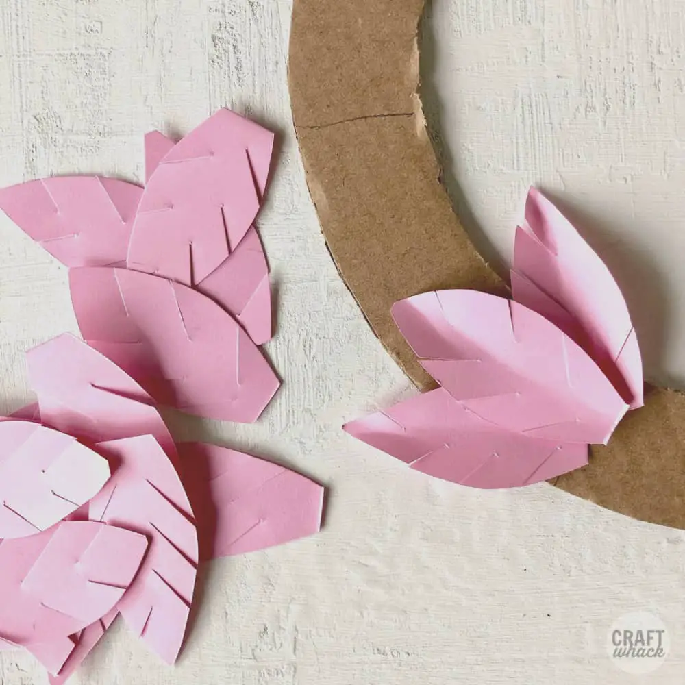 3 paper leaves being glued onto a cardboard wreath shape