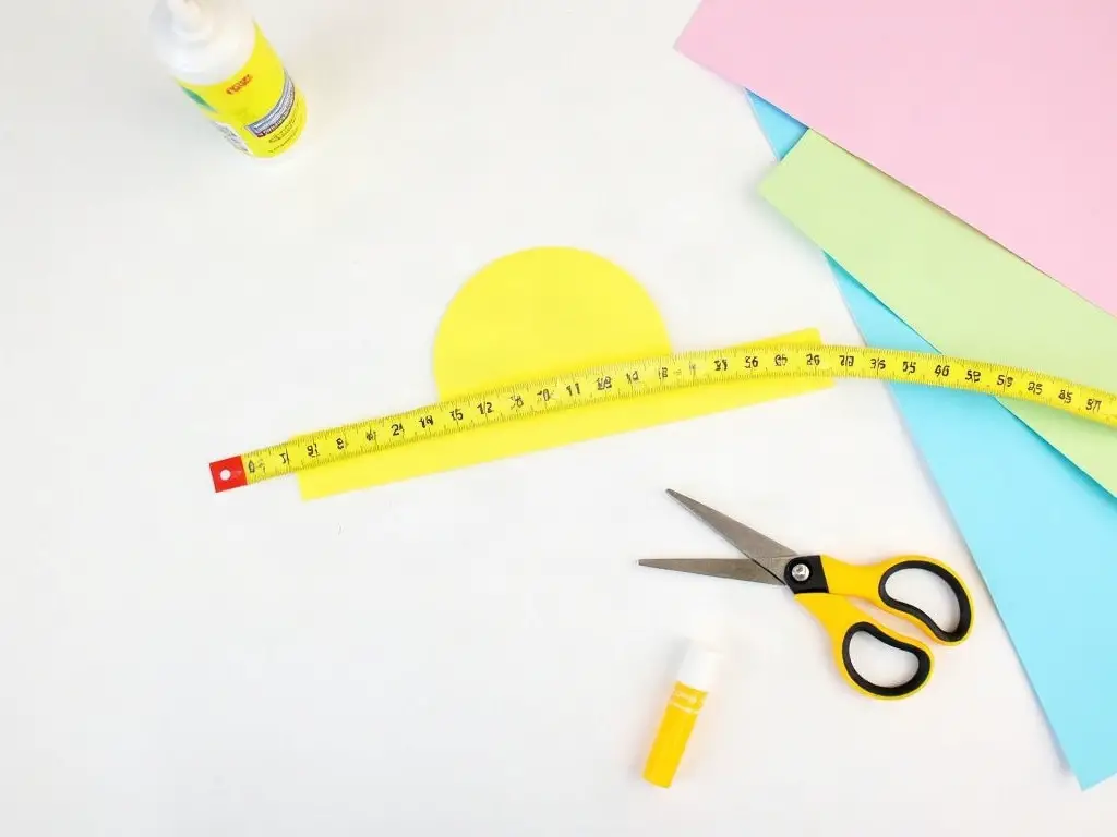 Paper strip, scissors, glue and construction paper laid out to make a crazy hat