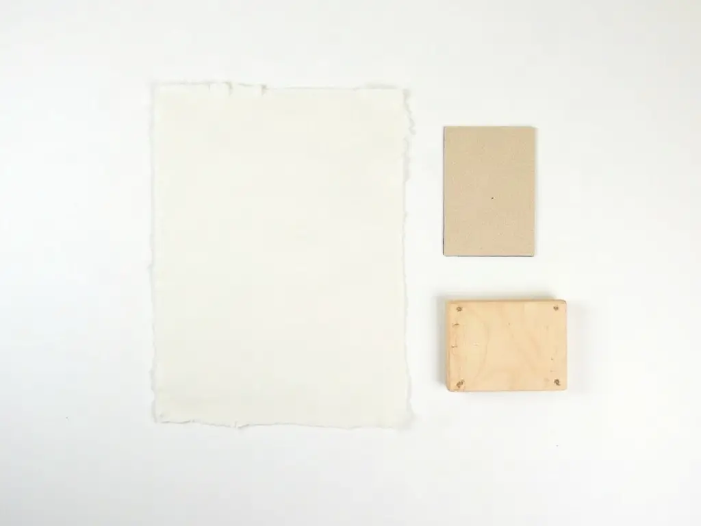 Freezer paper, scraper card, sandpaper and a wood board laid out for an image transfer